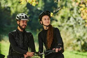 A blissful couple, adorned in professional cycling gear, enjoys a romantic bicycle ride through a park, surrounded by modern natural attractions, radiating love and happiness photo