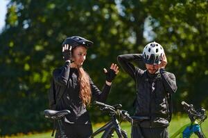 A sweet couple, equipped with bicycles and engrossed in coordinating their journey, checks their GPS mobile and watches while planning scenic routes in the park, seamlessly blending technology and photo
