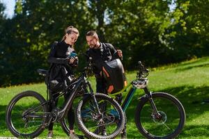 A sweet couple, equipped with bicycles and engrossed in coordinating their journey, checks their GPS mobile and watches while planning scenic routes in the park, seamlessly blending technology and photo