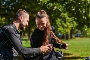 A sweet couple, equipped with bicycles and engrossed in coordinating their journey, checks their GPS mobile and watches while planning scenic routes in the park, seamlessly blending technology and photo
