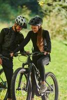 A sweet couple, equipped with bicycles and engrossed in coordinating their journey, checks their GPS mobile and watches while planning scenic routes in the park, seamlessly blending technology and photo