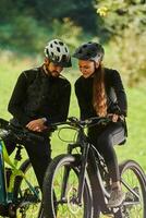 A sweet couple, equipped with bicycles and engrossed in coordinating their journey, checks their GPS mobile and watches while planning scenic routes in the park, seamlessly blending technology and photo