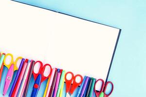 School supplies. Back to School design elements. Colorful markers and scissors on opened empty notepad on light blue paper background. photo