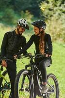 A sweet couple, equipped with bicycles and engrossed in coordinating their journey, checks their GPS mobile and watches while planning scenic routes in the park, seamlessly blending technology and photo