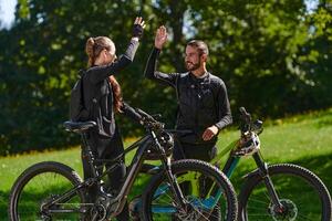 A sweet couple, equipped with bicycles and engrossed in coordinating their journey, checks their GPS mobile and watches while planning scenic routes in the park, seamlessly blending technology and photo