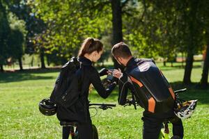 A sweet couple, equipped with bicycles and engrossed in coordinating their journey, checks their GPS mobile and watches while planning scenic routes in the park, seamlessly blending technology and photo