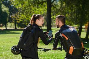 A sweet couple, equipped with bicycles and engrossed in coordinating their journey, checks their GPS mobile and watches while planning scenic routes in the park, seamlessly blending technology and photo