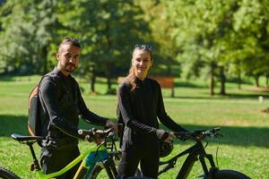A blissful couple, adorned in professional cycling gear, enjoys a romantic bicycle ride through a park, surrounded by modern natural attractions, radiating love and happiness photo