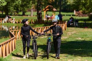 A blissful couple, adorned in professional cycling gear, enjoys a romantic bicycle ride through a park, surrounded by modern natural attractions, radiating love and happiness photo