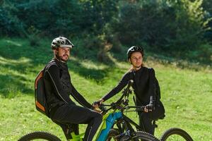A sweet couple, equipped with bicycles and engrossed in coordinating their journey, checks their GPS mobile and watches while planning scenic routes in the park, seamlessly blending technology and photo