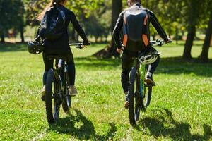 A blissful couple, adorned in professional cycling gear, enjoys a romantic bicycle ride through a park, surrounded by modern natural attractions, radiating love and happiness photo