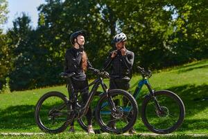 A sweet couple, equipped with bicycles and engrossed in coordinating their journey, checks their GPS mobile and watches while planning scenic routes in the park, seamlessly blending technology and photo