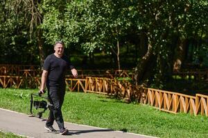 After completing a cinematic venture, a skilled videographer, adorned with camera equipment, leisurely strolls through the park, capturing the essence of post-production satisfaction and creative photo