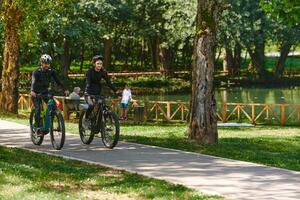 A blissful couple, adorned in professional cycling gear, enjoys a romantic bicycle ride through a park, surrounded by modern natural attractions, radiating love and happiness photo