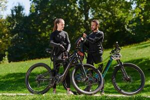 A sweet couple, equipped with bicycles and engrossed in coordinating their journey, checks their GPS mobile and watches while planning scenic routes in the park, seamlessly blending technology and photo