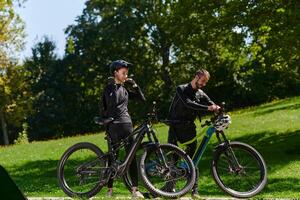 A sweet couple, equipped with bicycles and engrossed in coordinating their journey, checks their GPS mobile and watches while planning scenic routes in the park, seamlessly blending technology and photo