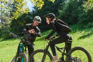 A sweet couple, equipped with bicycles and engrossed in coordinating their journey, checks their GPS mobile and watches while planning scenic routes in the park, seamlessly blending technology and photo