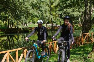 A blissful couple, adorned in professional cycling gear, enjoys a romantic bicycle ride through a park, surrounded by modern natural attractions, radiating love and happiness photo