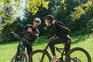 A sweet couple, equipped with bicycles and engrossed in coordinating their journey, checks their GPS mobile and watches while planning scenic routes in the park, seamlessly blending technology and photo