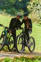 A sweet couple, equipped with bicycles and engrossed in coordinating their journey, checks their GPS mobile and watches while planning scenic routes in the park, seamlessly blending technology and photo