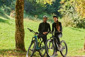 A sweet couple, equipped with bicycles and engrossed in coordinating their journey, checks their GPS mobile and watches while planning scenic routes in the park, seamlessly blending technology and photo