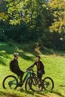 A sweet couple, equipped with bicycles and engrossed in coordinating their journey, checks their GPS mobile and watches while planning scenic routes in the park, seamlessly blending technology and photo