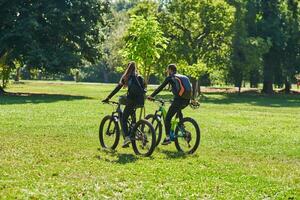 A blissful couple, adorned in professional cycling gear, enjoys a romantic bicycle ride through a park, surrounded by modern natural attractions, radiating love and happiness photo