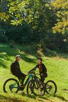 A sweet couple, equipped with bicycles and engrossed in coordinating their journey, checks their GPS mobile and watches while planning scenic routes in the park, seamlessly blending technology and photo