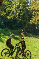 A sweet couple, equipped with bicycles and engrossed in coordinating their journey, checks their GPS mobile and watches while planning scenic routes in the park, seamlessly blending technology and photo