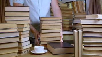 A bearded man reads a book in the library. Stacks of books and cup of tea on table. Concept of Reading and Education. video