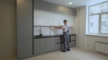 The builder checks the dimensions and quality of installation of the kitchen furniture structure. Professional worker in uniform in a new apartment. Production and installation of new furniture. video