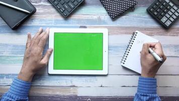 A man using a tablet with a green screen on a wooden desk video