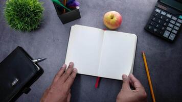 A man's hands holding an open notebook with a pencil and an apple on a desk video