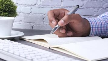 A man writing in a notebook with a pen on a desk video