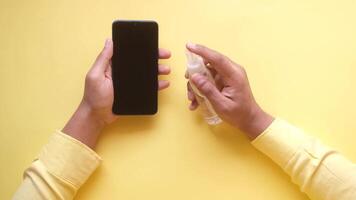 A woman's hands holding a smartphone and a bottle of hand sanitizer on a yellow background video