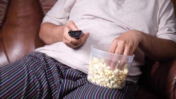 A man sitting on a couch with a bowl of popcorn and a remote control video