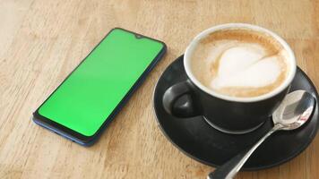 A smartphone with green screen and a cup of cappuccino on a wooden table video
