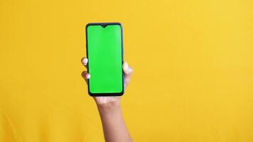 Hand holding smartphone with green screen on yellow background video