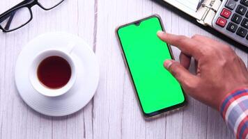 Man using smartphone with green screen on wooden table with cup of coffee and calculator video