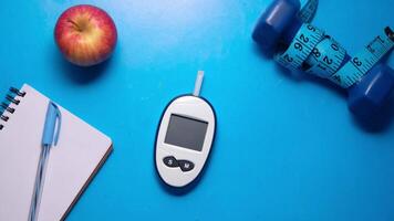 Diabetes and health concept with glucose meter, apple, and notebook on blue background video