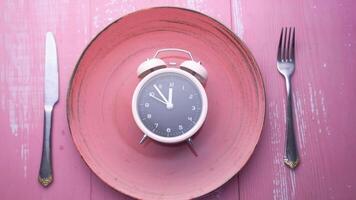 An alarm clock sits on a pink plate with silverware video