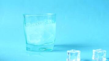 A glass of ice water with ice cubes on a blue background video