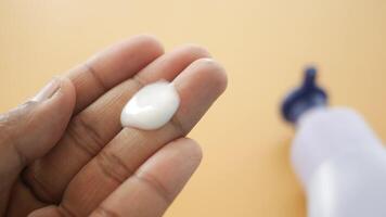 A hand is holding some cream on its palm, while a bottle is placed in the background video