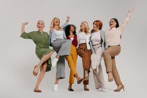 Multi-ethnic group of happy mature women embracing and dancing against grey background photo