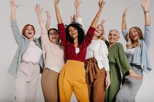 Multi-ethnic group of happy mature women gesturing and smiling against grey background photo