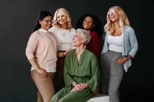 Multi-ethnic group of confident mature women bonding and smiling against black background photo