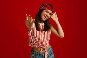Happy young hipster woman gesturing and smiling while standing on red background photo