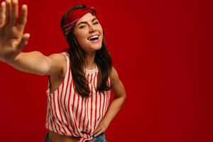 Happy young hipster woman stretching out hand and smiling while standing on red background photo