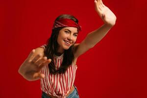 Happy young hipster woman stretching out hands and smiling while standing on red background photo
