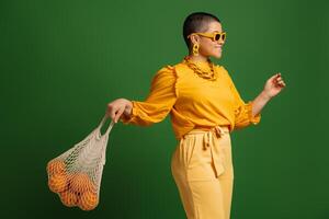 Playful young short hair woman carrying mesh bag with oranges against green background photo